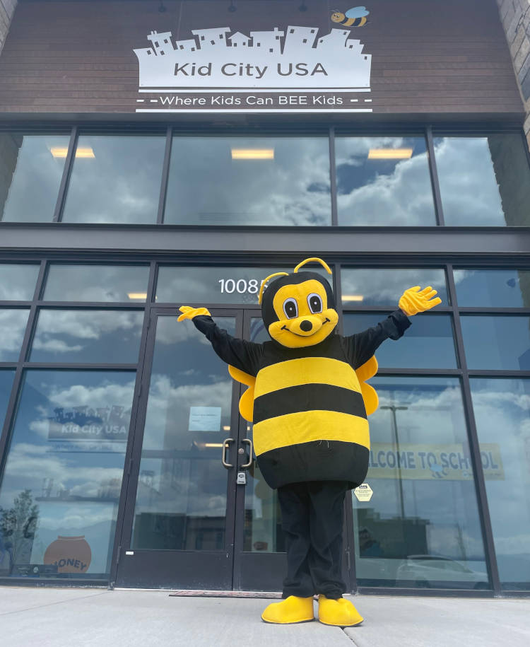 Mr. Bee, the Kid City USA Daycare mascot, standing proudly in front of the entrance of one of our centers, welcoming children with a warm and friendly smile.