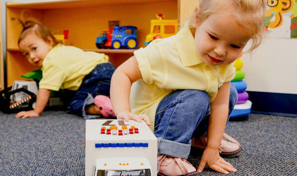 In our 2-year-old daycare class: Girl happily plays with toy truck, fostering early development and joyful exploration.